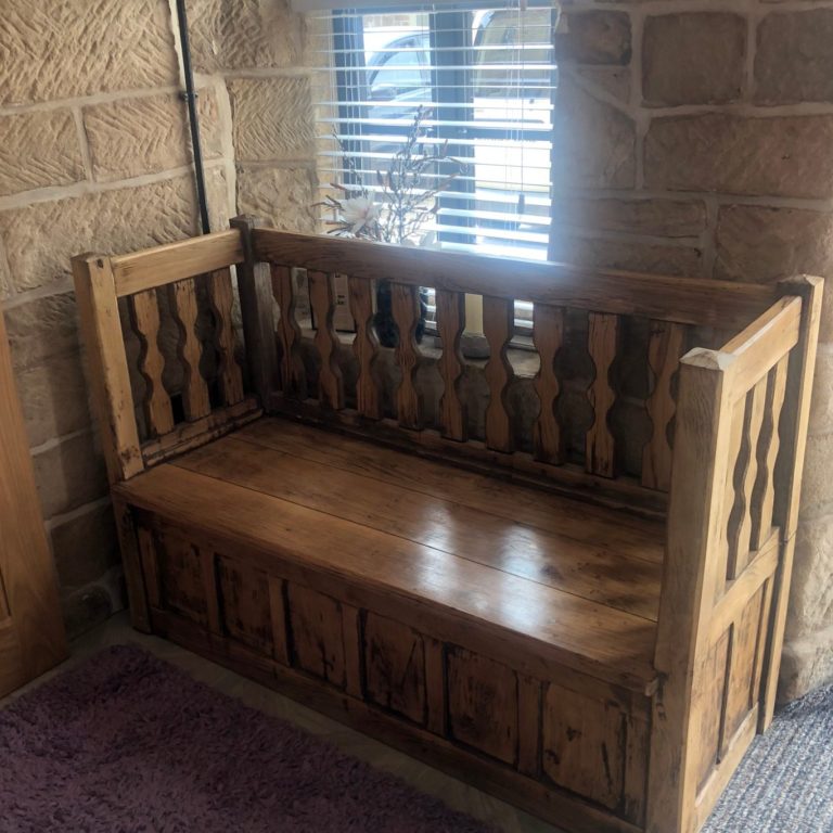 Wooden bench with a slatted backrest, placed against a stone wall near a window.